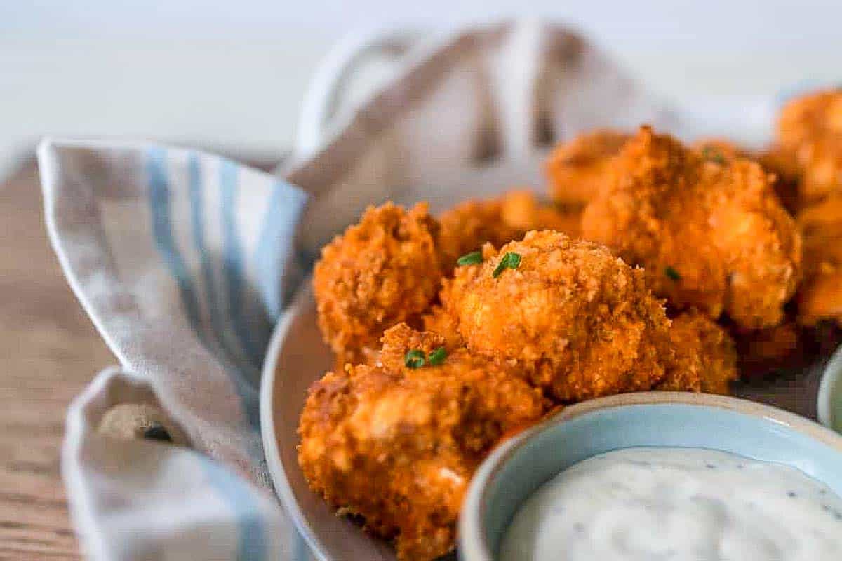 sourdough battered buffalo cauliflower wings in a tray with dippings sauce. Plate is on a blue and cream napkin
