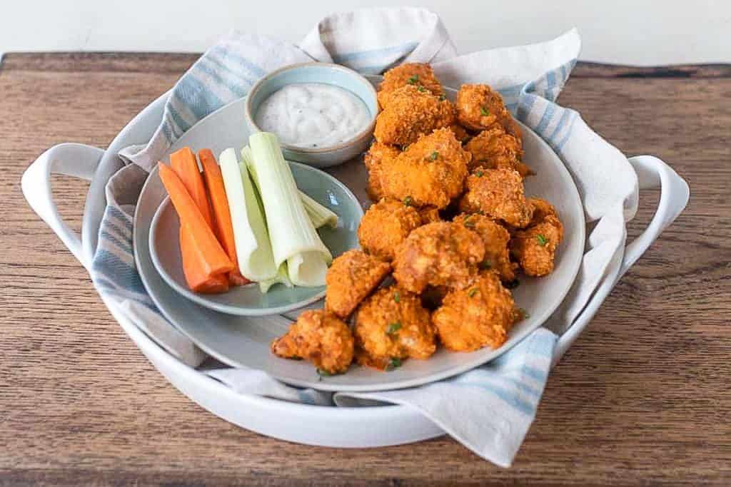 sourdough battered buffalo cauliflower wings on a plate with celery, carrots, and a Caesar dipping sauce on a place on top of a napkin lined tray