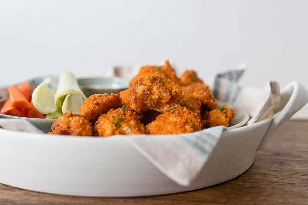 side view of a serving tray lined with a napkin and a plate full of buffalo cauliflower bites