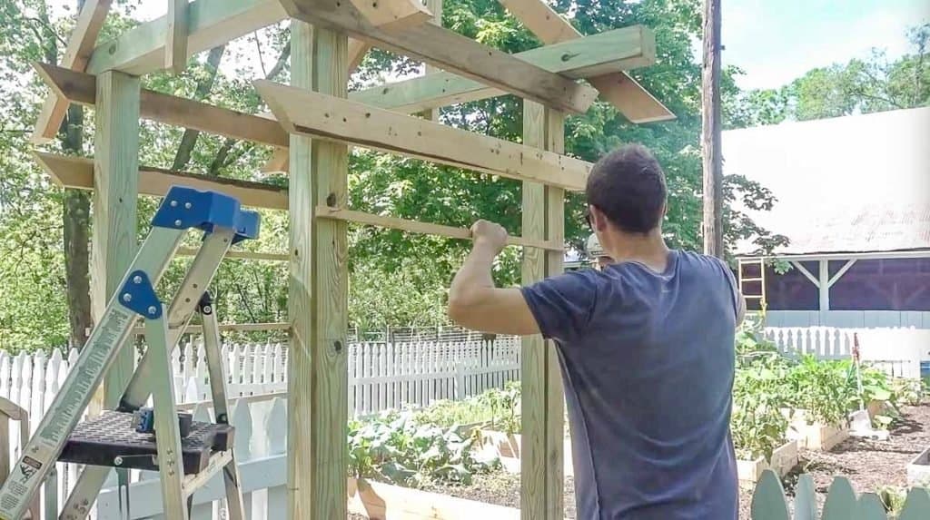 man acting cross strips of wood on an arbor as a trellis