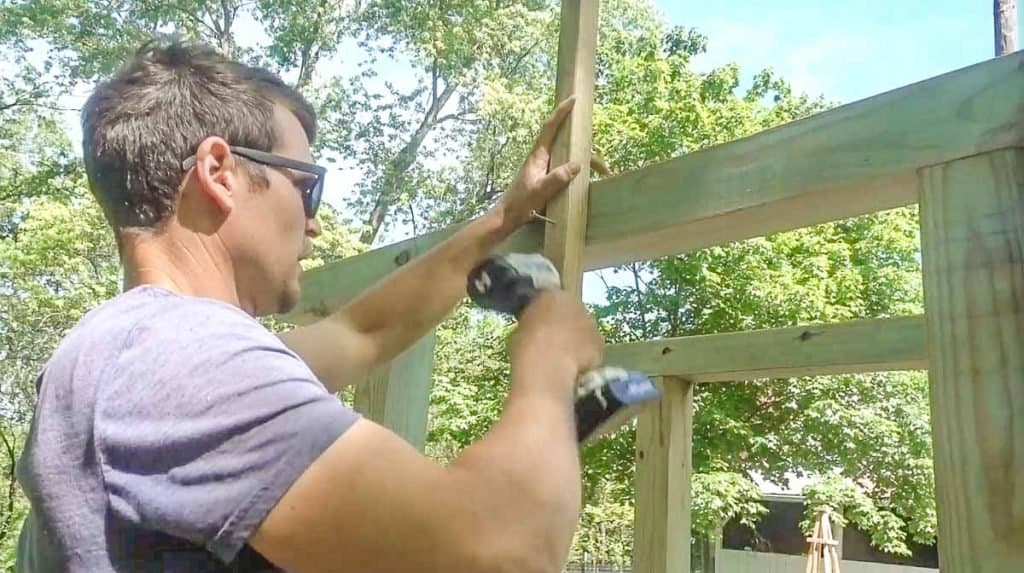 man wearing blue shirt drilling a 1x1 into an arbor frame to create the roof