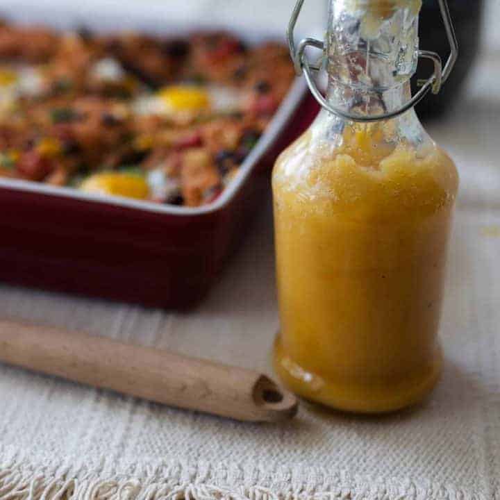 fermented hot sauce in a glass bottle with a swing top lid. A baking dish with hash in the background