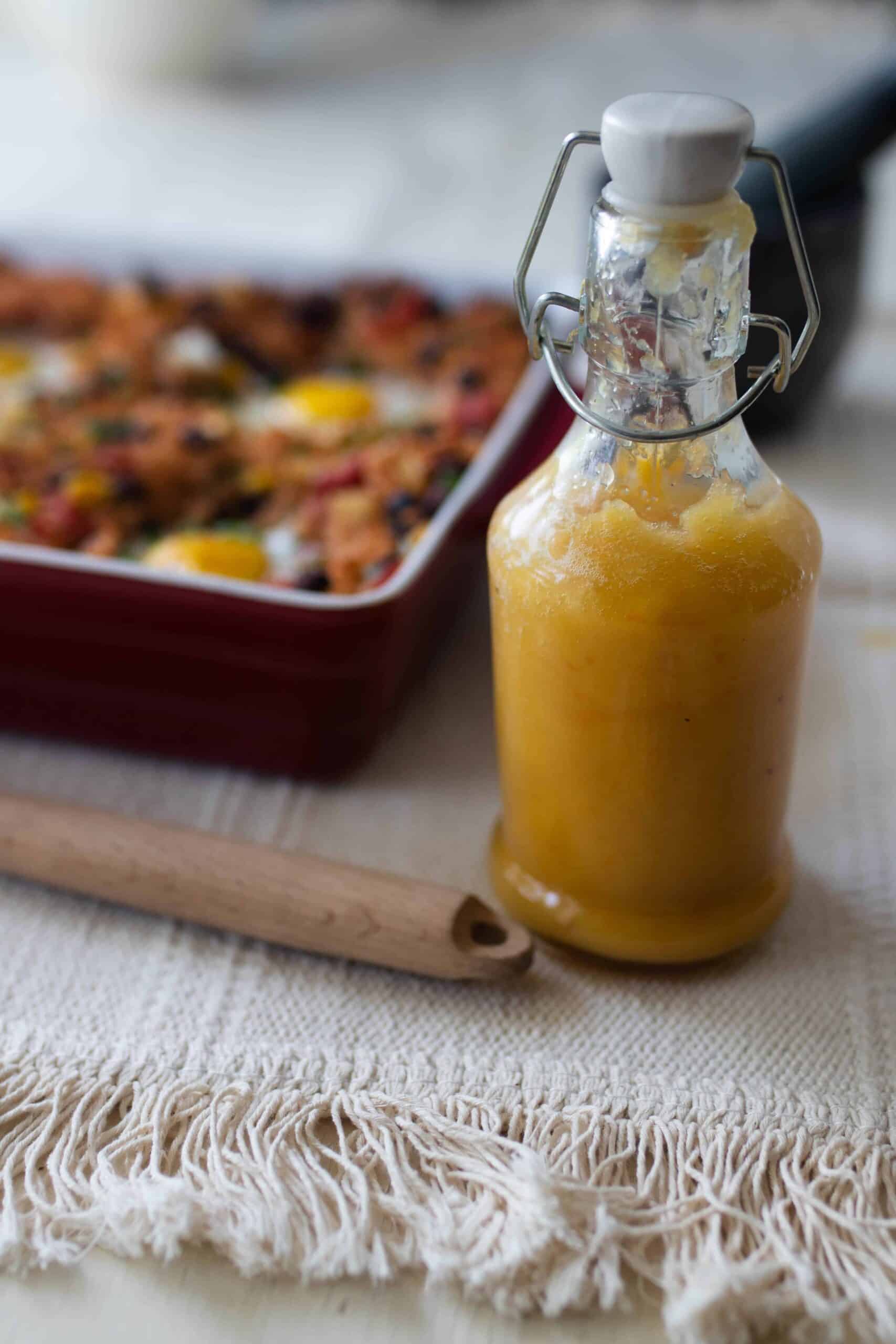 fermented hot sauce in a glass bottle with a swing top lid. A baking dish with hash in the background