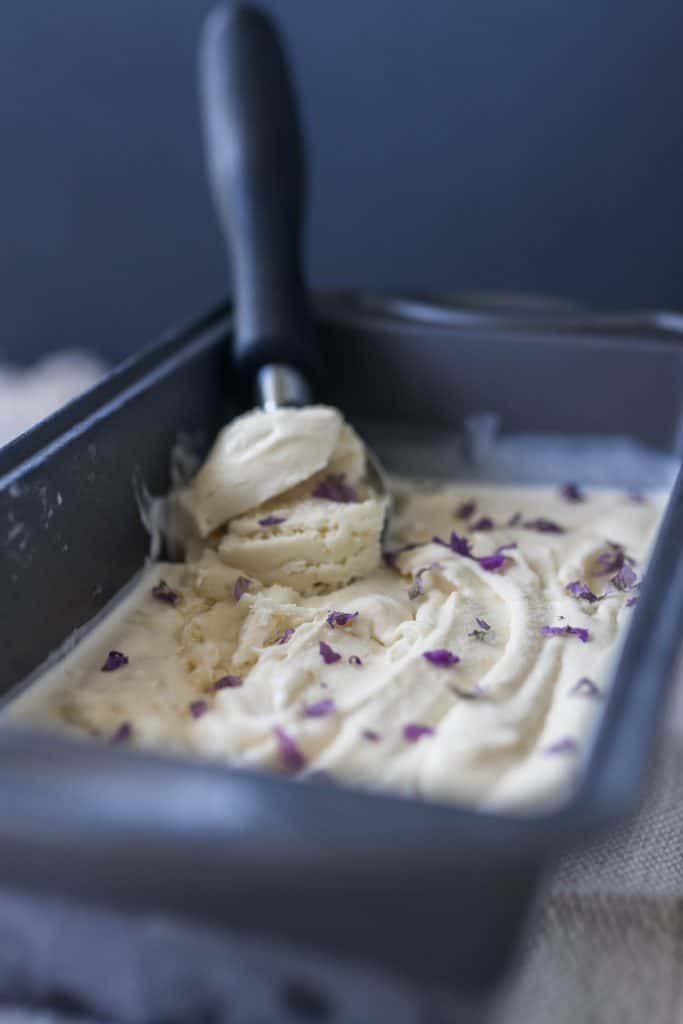 lavender ice cream in a bread loaf pan with a ice cream scoop in the ice cream