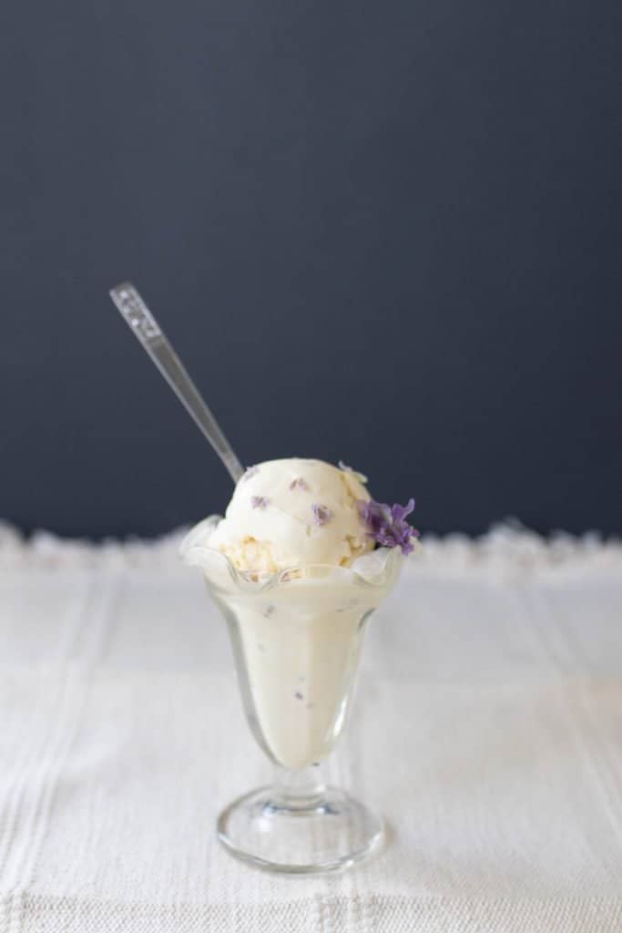 lavender and honey ice cream in a glass Sunday cup with fresh lavender flowers. A spoon is placed in the ice cream,