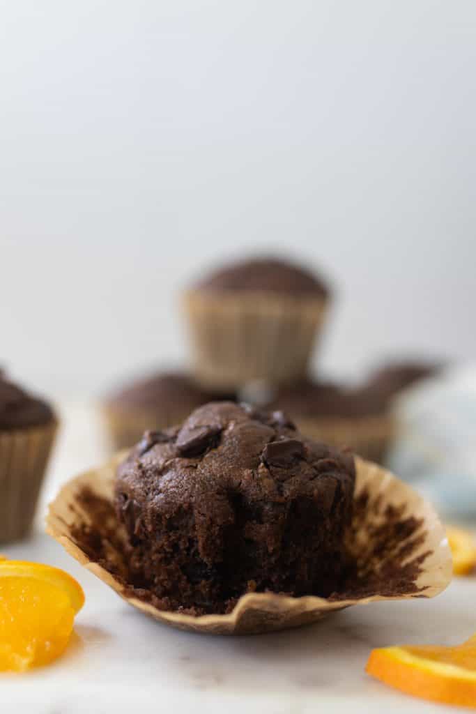 chocolate zucchini muffins with the muffin liner peeled off, orange slices around the muffin and more muffins in the background