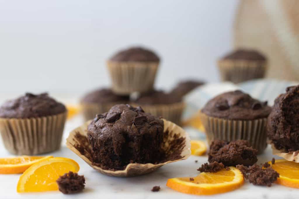 sourdough chocolate zucchini muffins on a countertop with sliced oranges