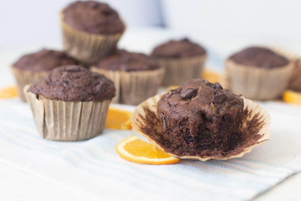 chocolate zucchini muffins placed on a white countertop with orange slices around the muffins