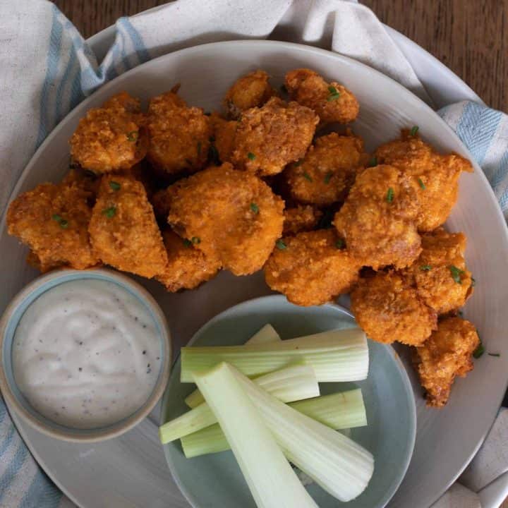 sourdough battered buffalo cauliflower wings on a gray plate with a side of teaser dipping sauce and a bowl full of celery sticks