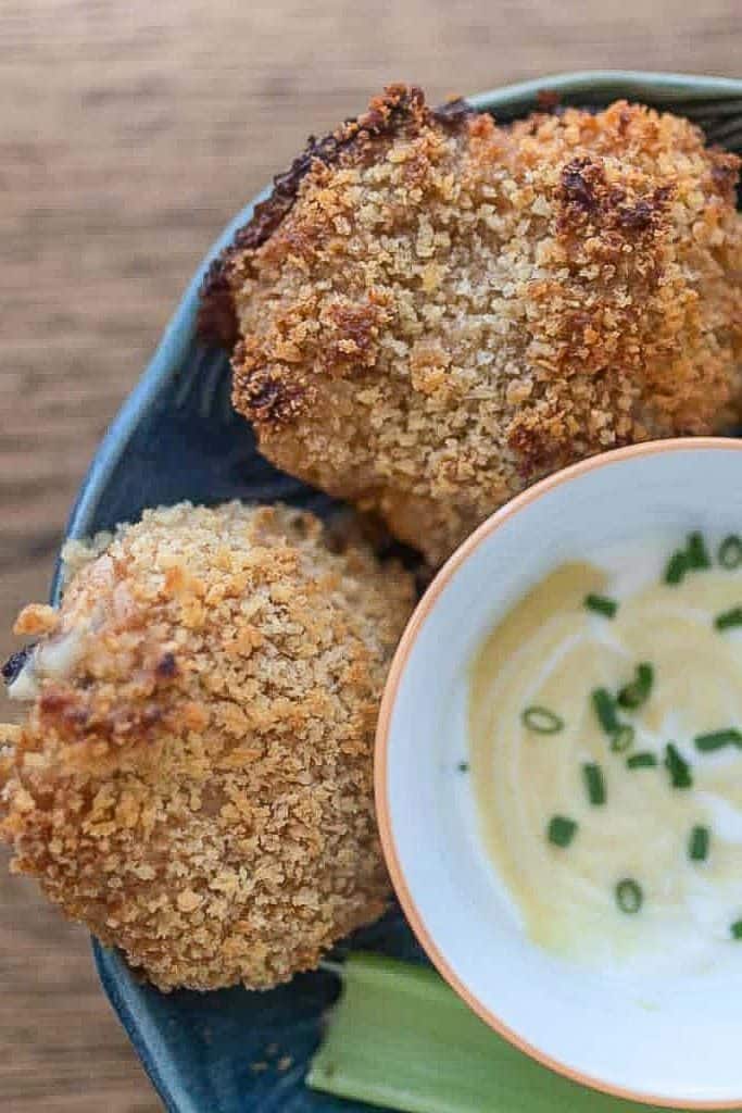 Close up with two sourdough oven-fried chicken thighs in a blue bowl with dipping sauce to the right in a bowl