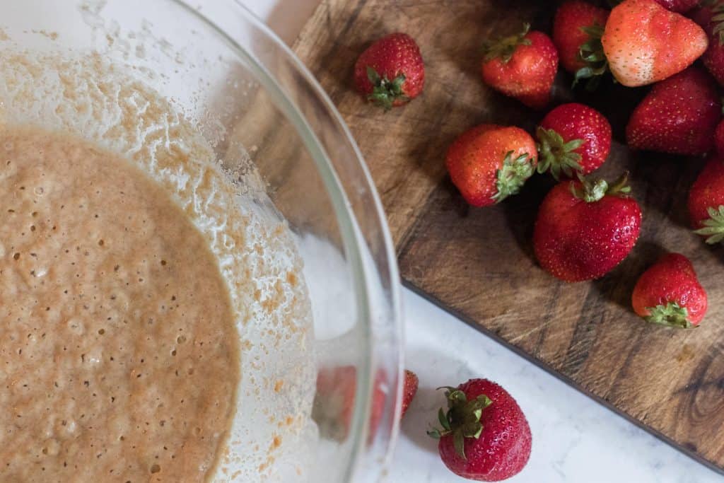 sourdough cobbler batter in a glass bowl. Fresh strawberries to the right on a wood cutting board