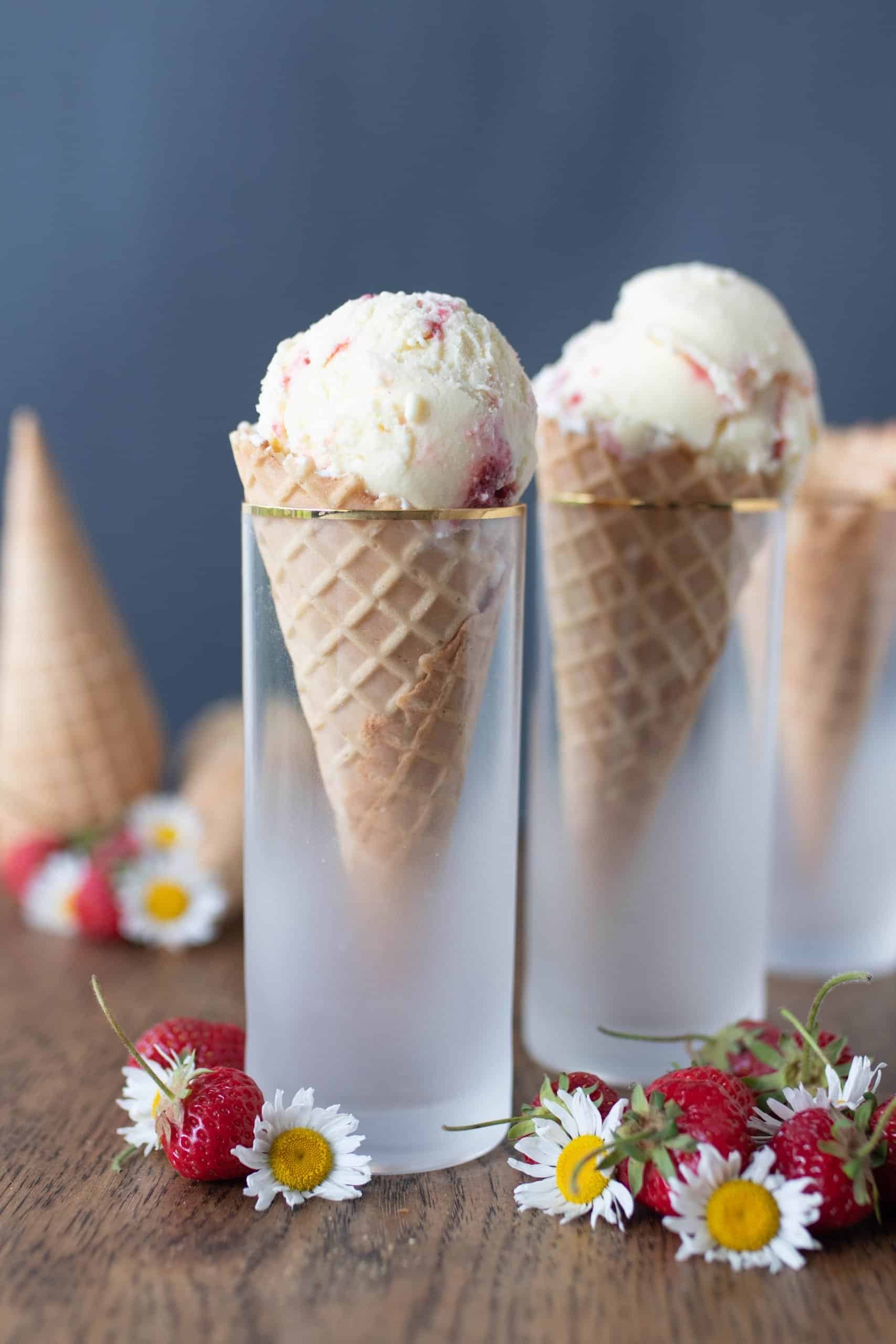 cones filled with strawberry cheesecake ice cream in cones in glasses on a wood table with strawberries and flowers spread across the table