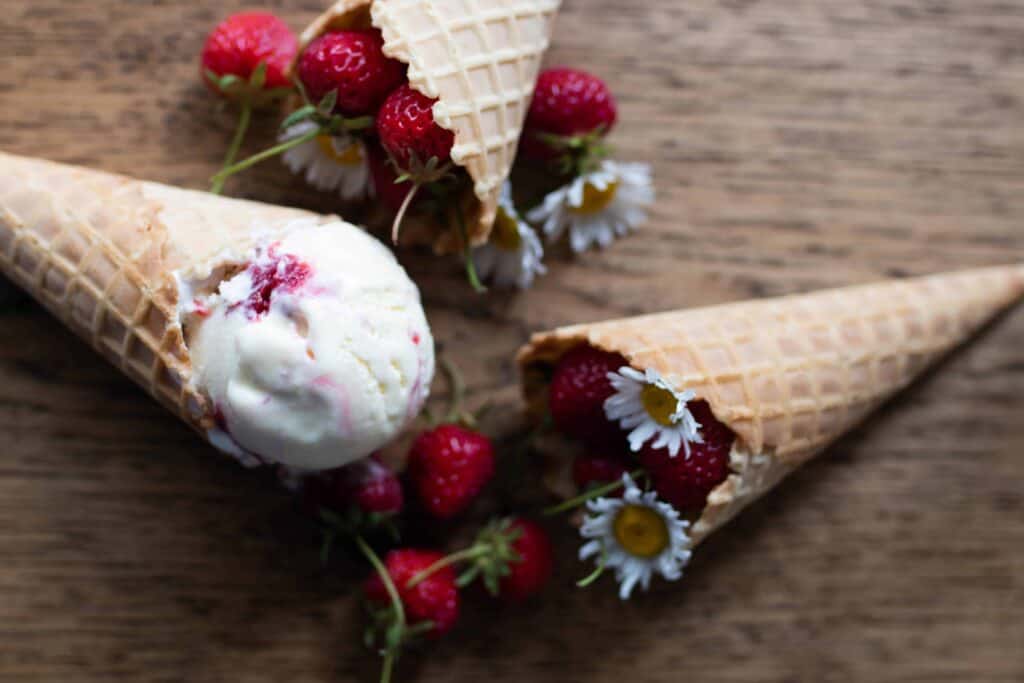 strawberry goat cheese ice cream in a cone on the left. more cones with fresh strawberries and flowers to the right