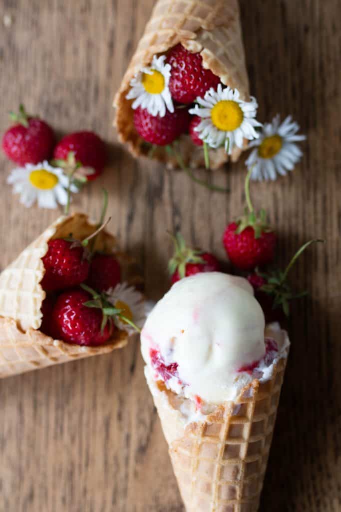 strawberry goat cheese ice cream in a cove with two more cones filled with strawberries with flowres