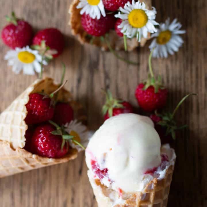 strawberry goat cheese ice cream in a cove with two more cones filled with strawberries with flowres