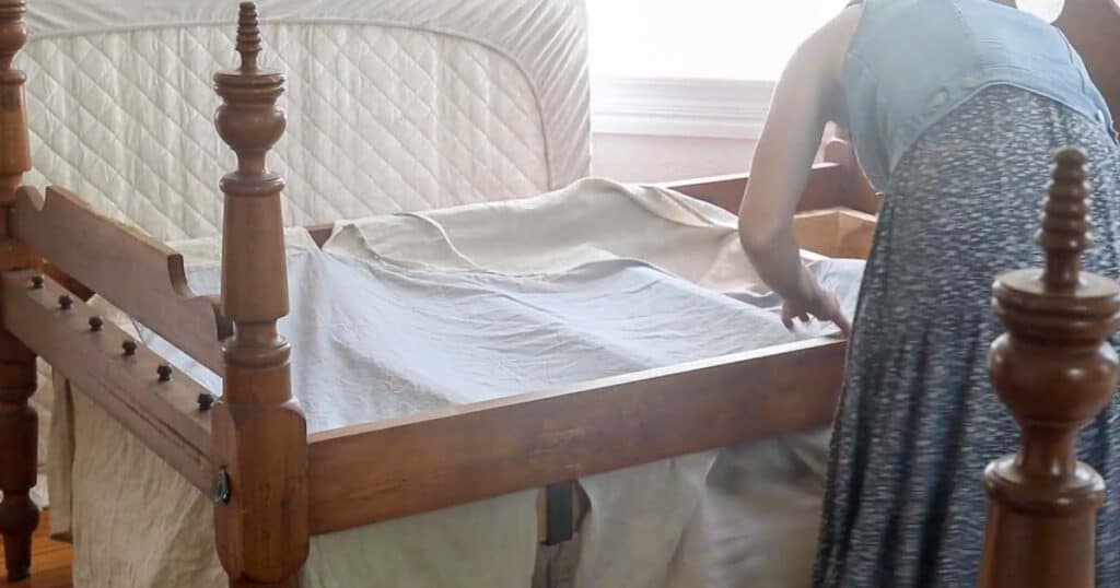 women placing a DIY beds skirt onto a antique bed to make sure it fits