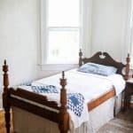 antique wooden bed with a white bedspread, blue and white build near the footboard and a linen bed skirt