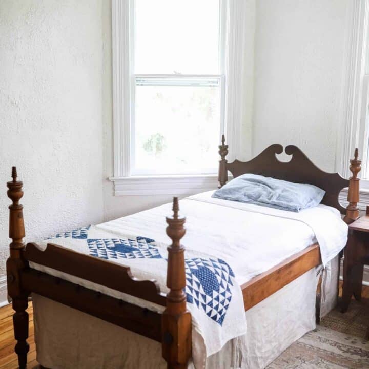 antique wooden bed with a white bedspread, blue and white build near the footboard and a linen bed skirt