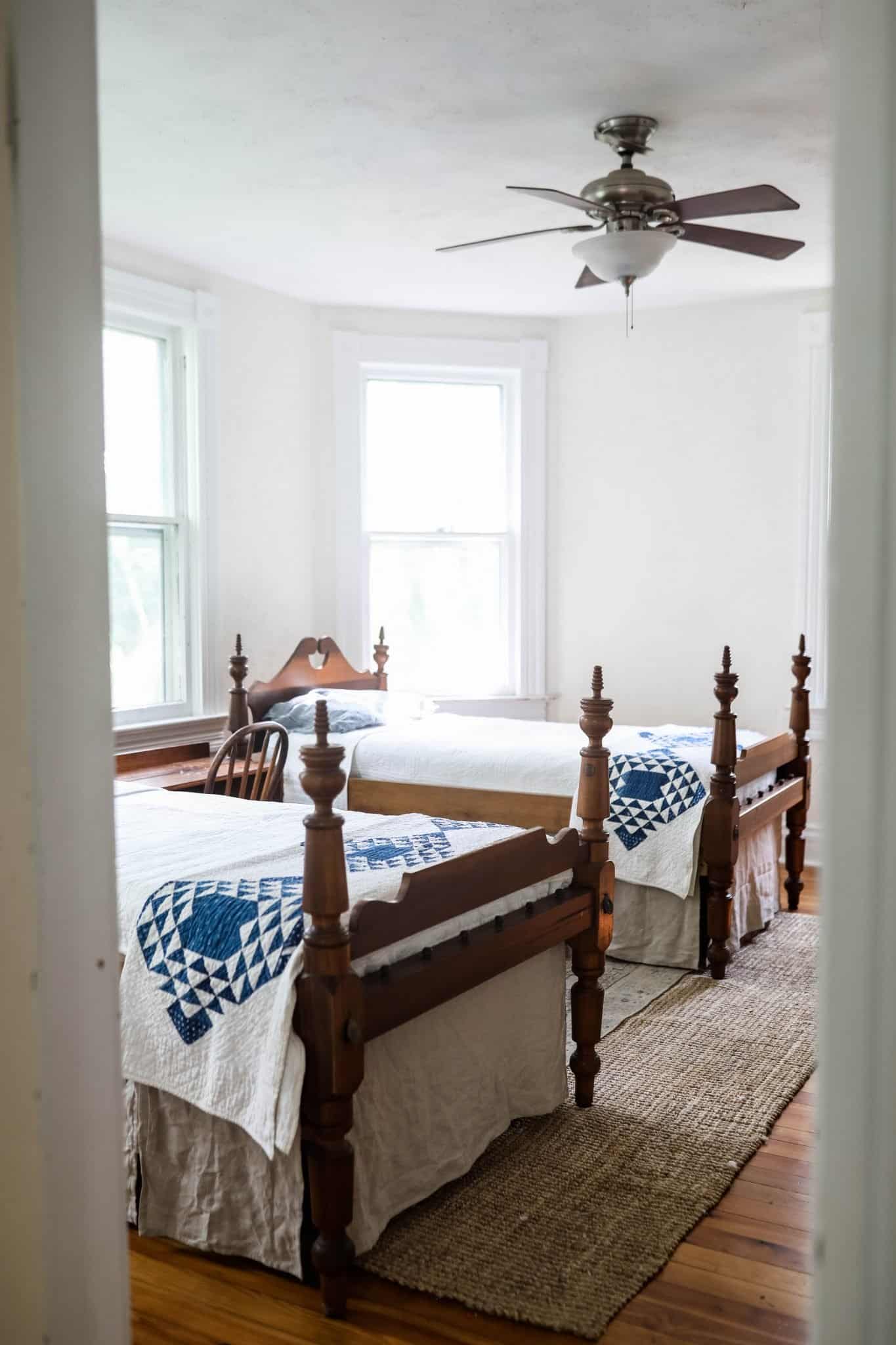 two antique wooden beds with linen bed skirts and blue and white quilts near the end of the bed