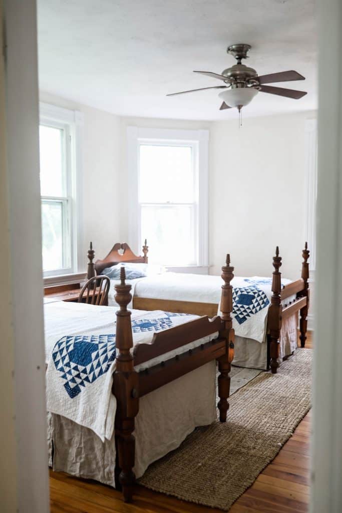 two antique wooden beds with linen bed skirts and blue and white quilts near the end of the bed