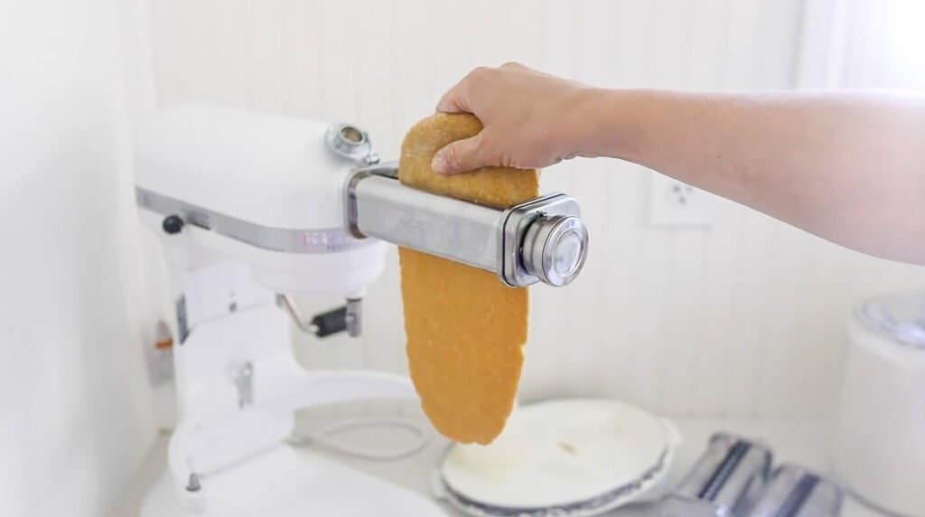 pasta dough being put through a pasta maker attachment on a stand mixer