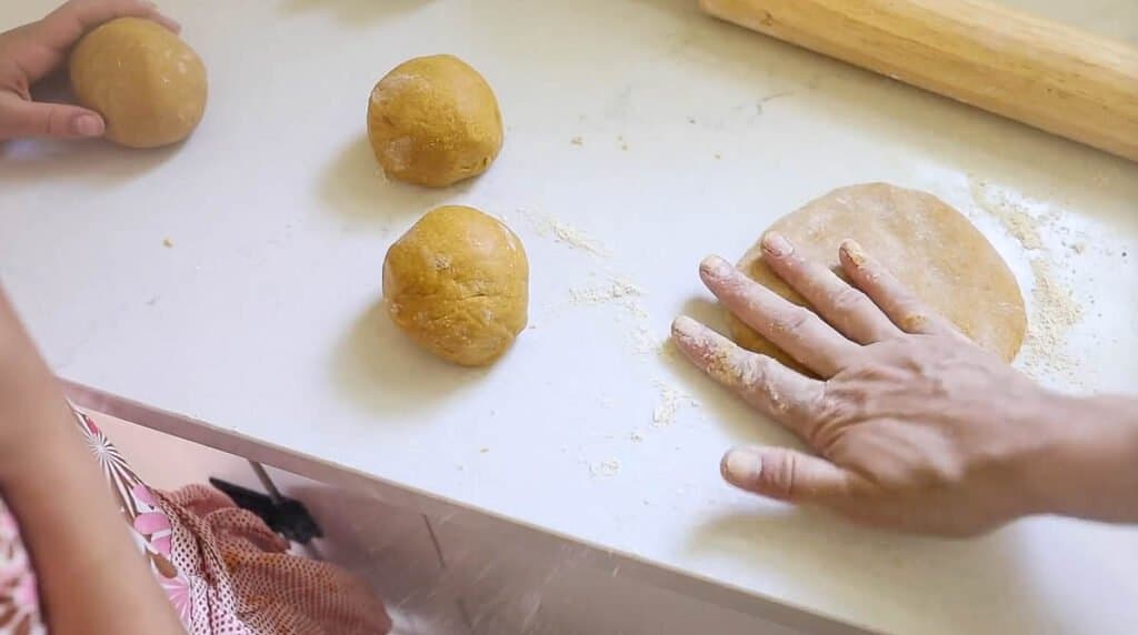 hand patting out pasta dough on a white counter top 