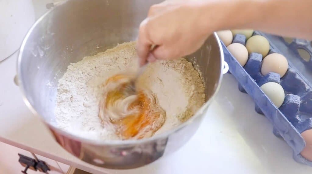 hand whisking eggs with a fork in a bowl of flour