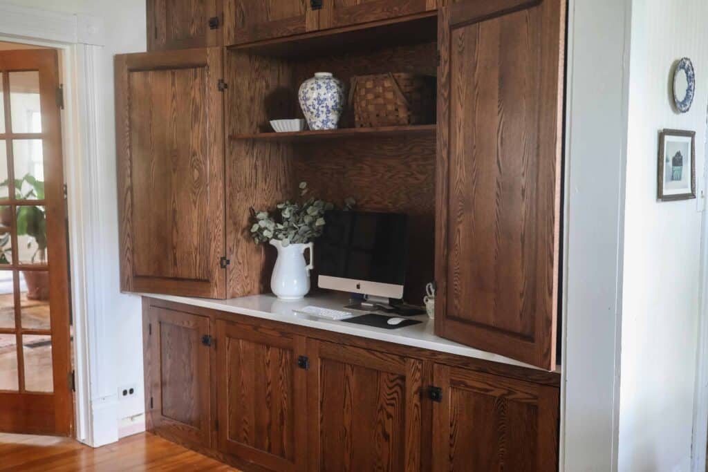 Custom floor to ceiling wood cabinetry with a quartz countertop desk area. Two doors are open revealing an organized office space