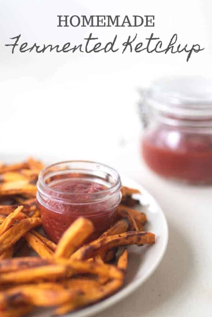 glass jar of homemade ketchup on a white plate with fries with a swing top jar of ketchup in the background