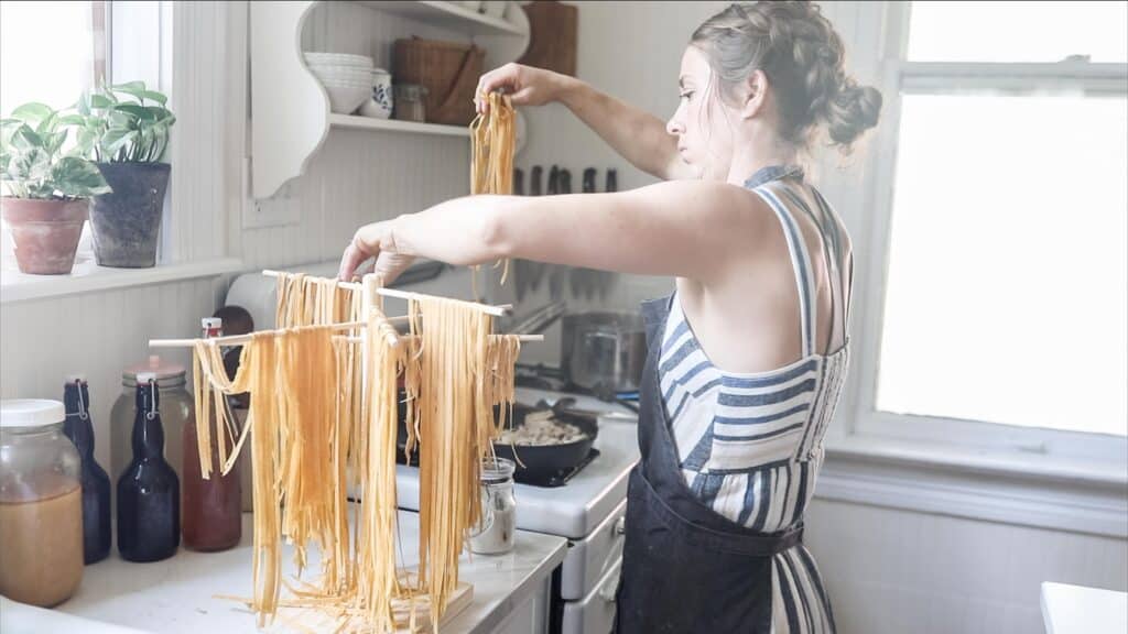 women adding homemade einkorn pasta from a pasta drying rack to a pot of boiling water