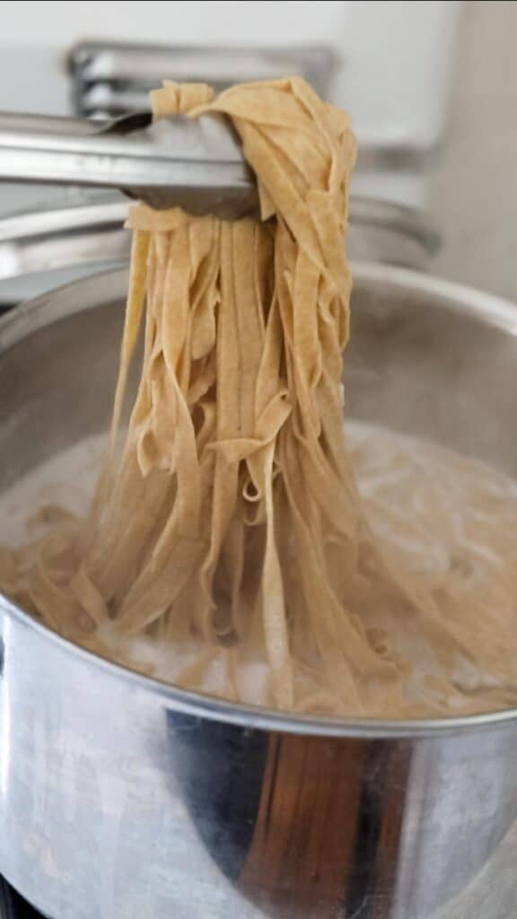 cooking fresh pasta with tongs pulling pasta out of pot of boiling water