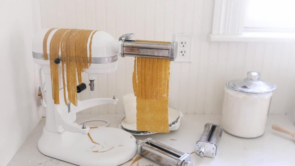 fresh pasta dough being cut with a pasta cutting attachment on a stand mixer