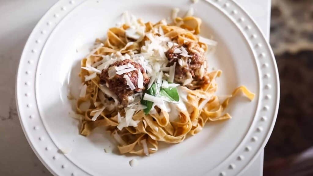 fresh homemade einkorn pasta on a white plate and topped with meatballs fresh herbs and cheese