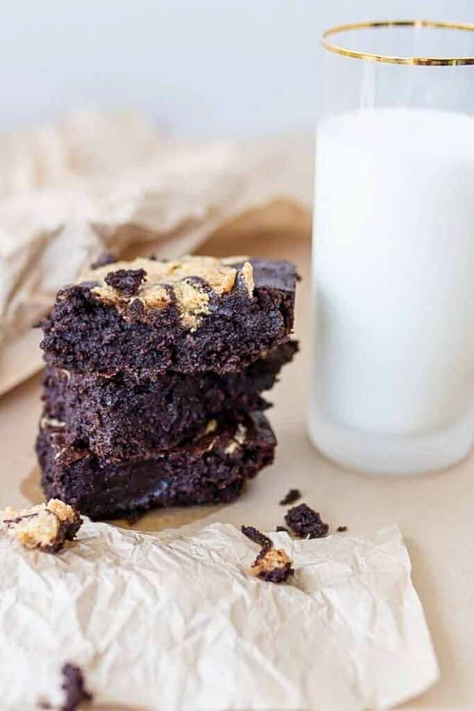 three sourdough brownies stacked up on parchment paper with a glass of milk to the right