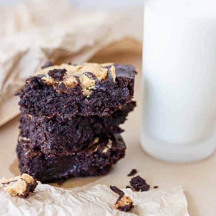 three sourdough brownies stacked up on parchment paper with a glass of milk to the right