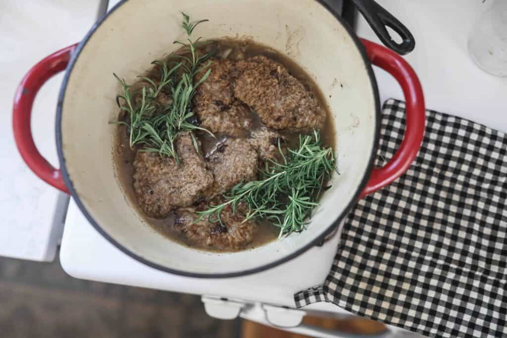 round steak with fresh rosemary, onions, and mushrooms in a red dutch oven
