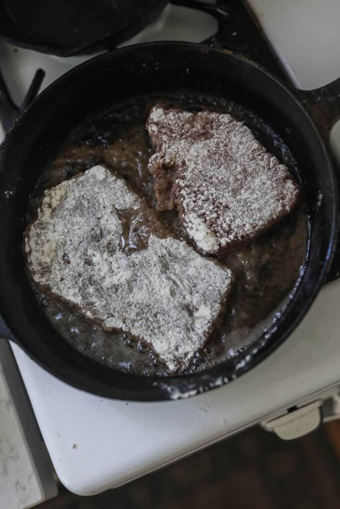 round steak dredged in flour and browning in a cast iron skillet with coconut oil