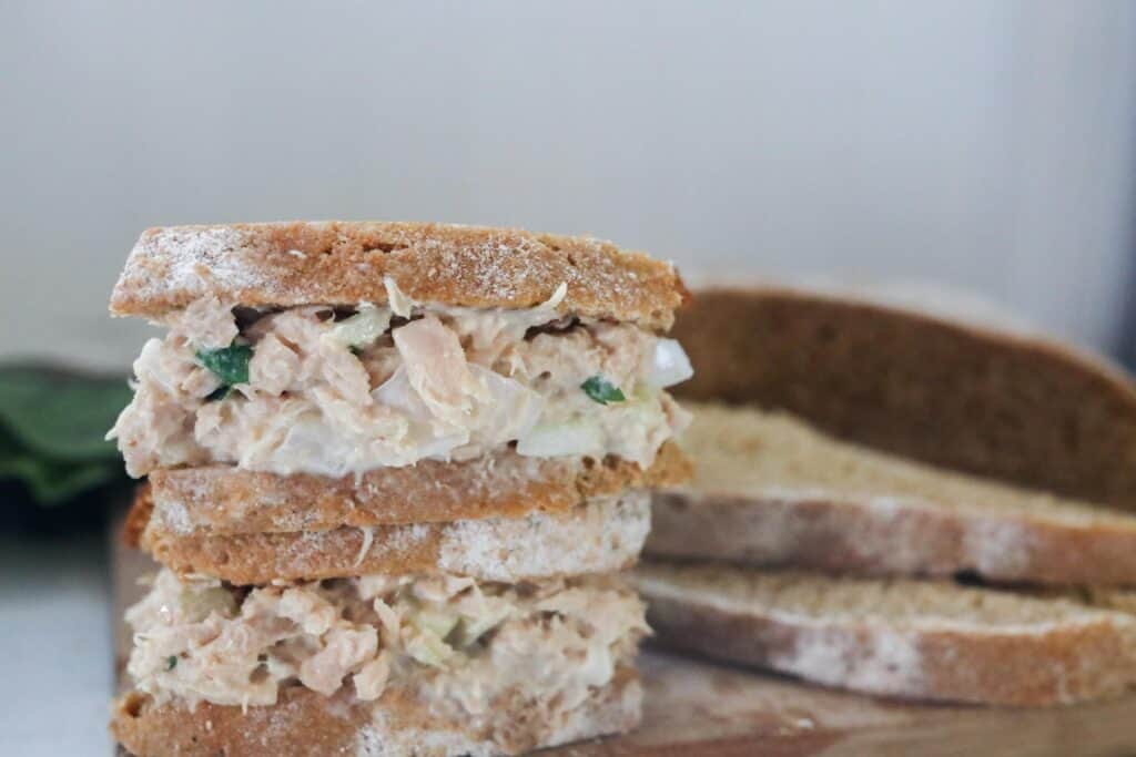 two tuna salad sandwiches stacked up with bread to the right