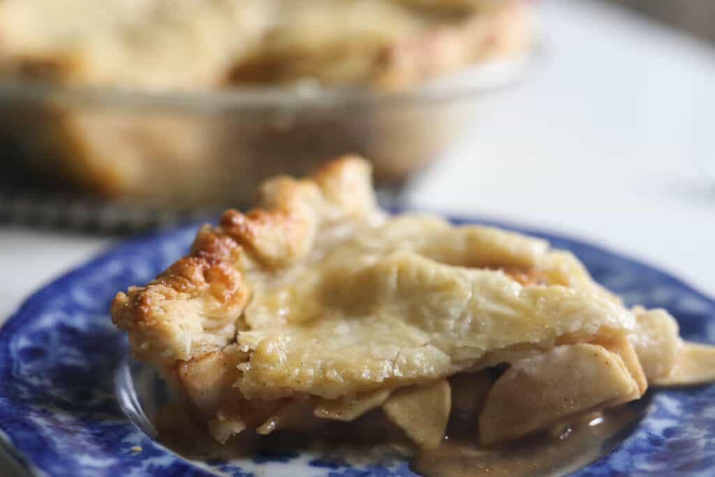 side view of a slice of apple pie with sourdough crust on a white and blue antique plate.