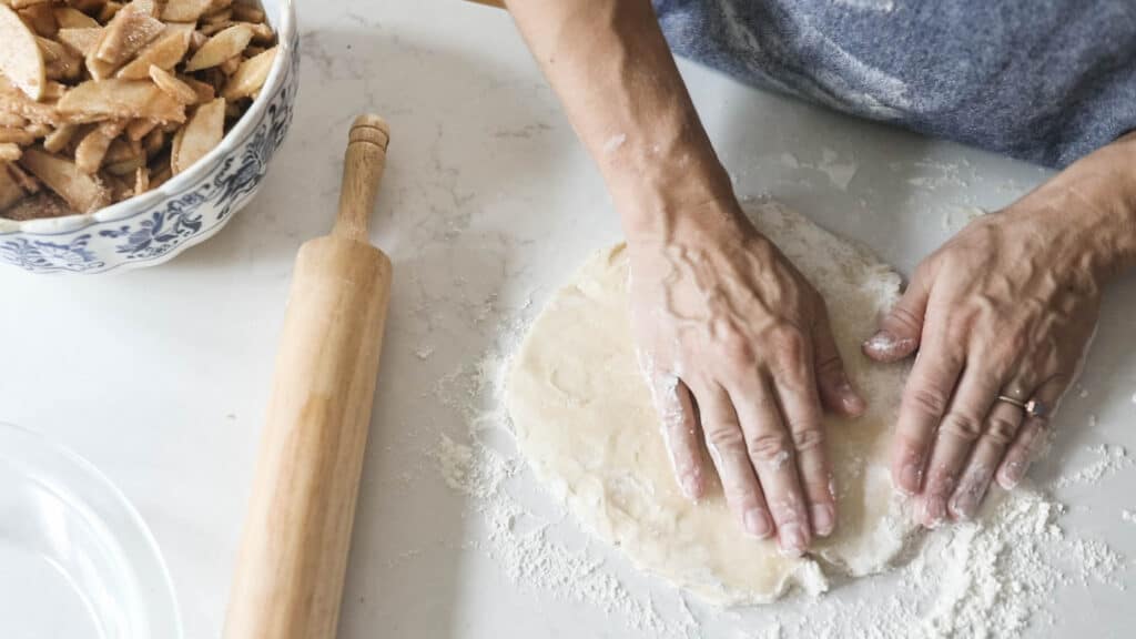 hands patting down pie crust on a floured countertop