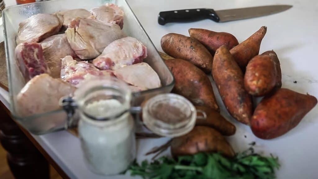 whole chicken cut up into sections in a baking dish with sweet potatoes to the right