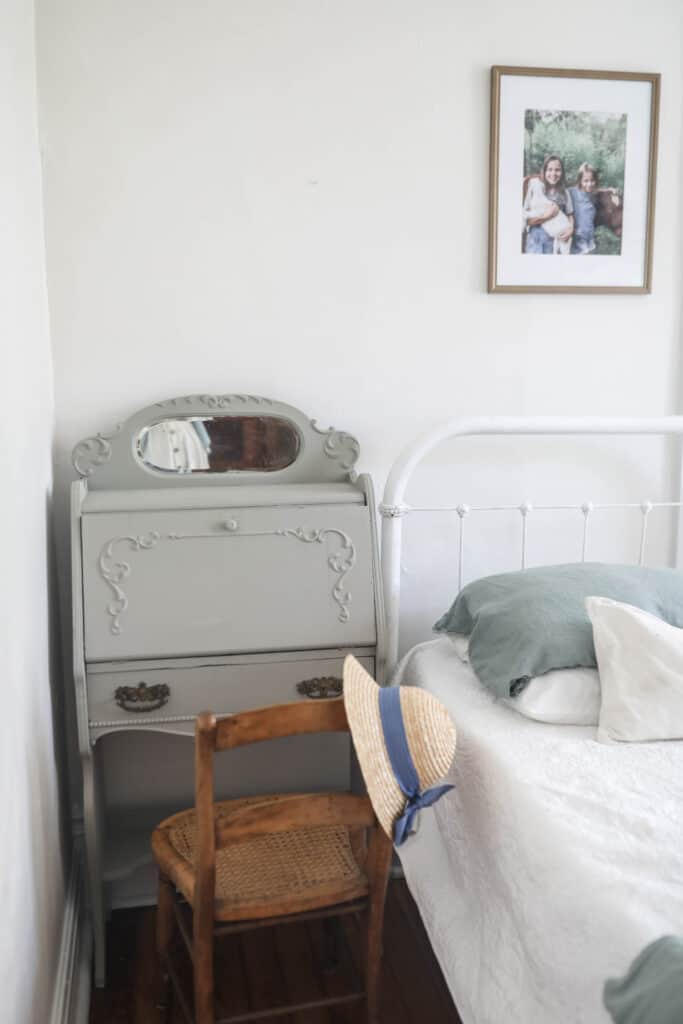 vintage secretary desk painted a beige color next to a white metal bed