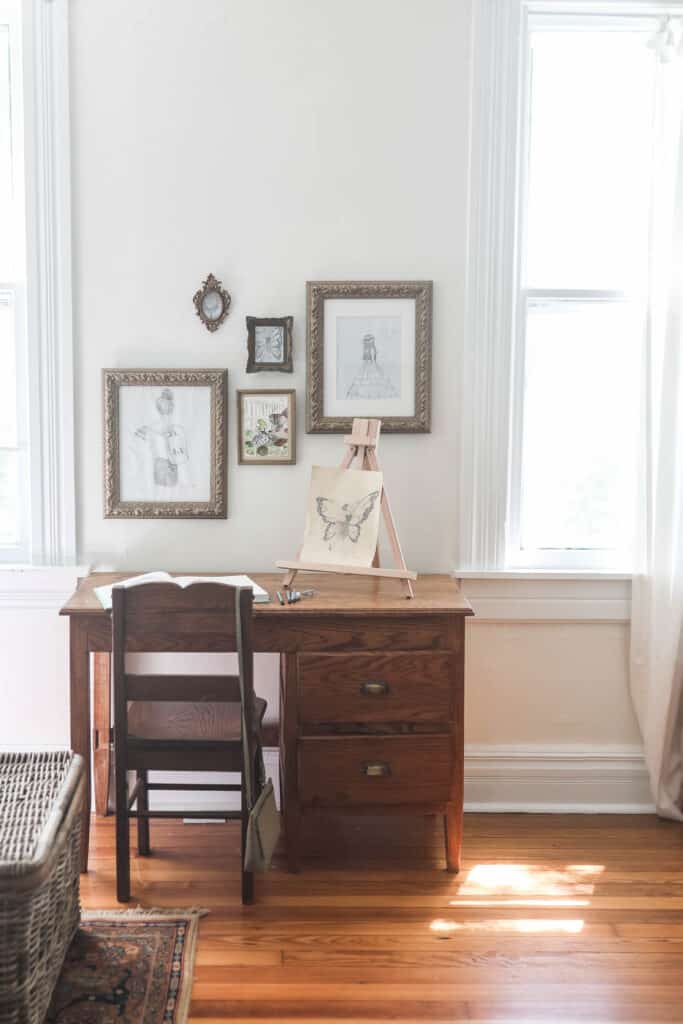 handmade wooden desk with brass handles. Gallery wall of drawings in gold frames are above the desk