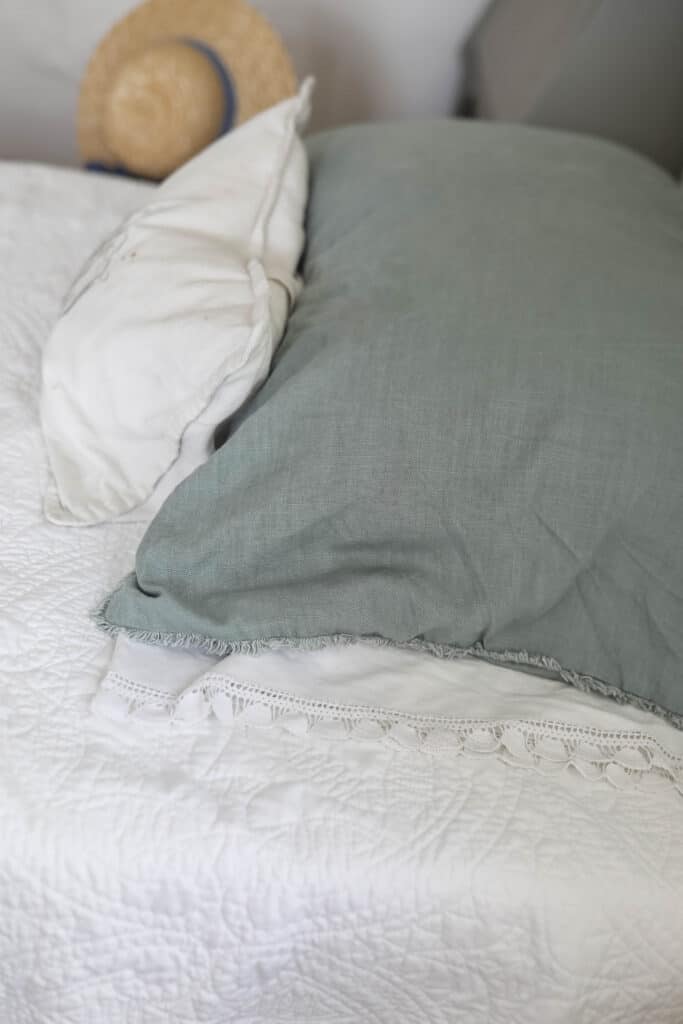 close up of a sage green linen pillow on top a vintage lace pillow