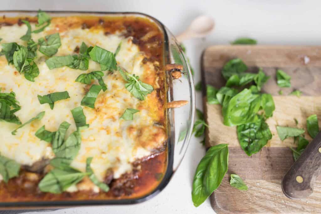 zucchini lasagna in a baking dish covered with fresh basil. A cutting board to the right with basil