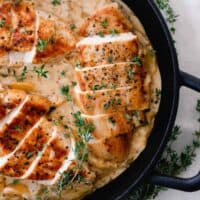 seared chicken breasts in a creamy peach sauce topped with herbs in a cast iron skillet