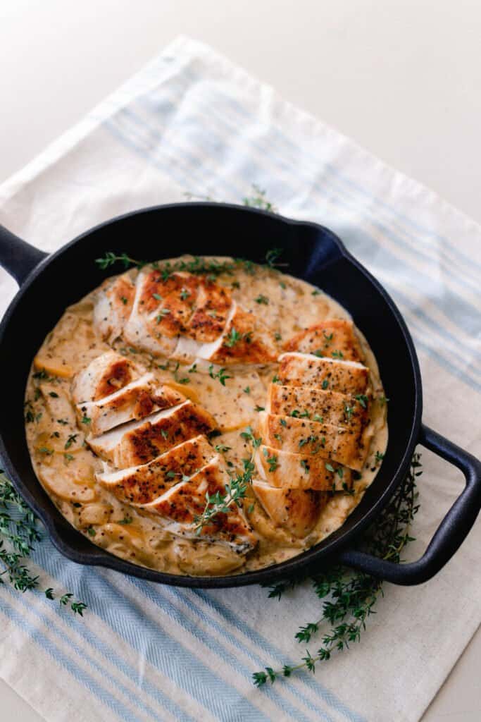 cast iron skillet with chicken and a creamy sauce with fresh thyme