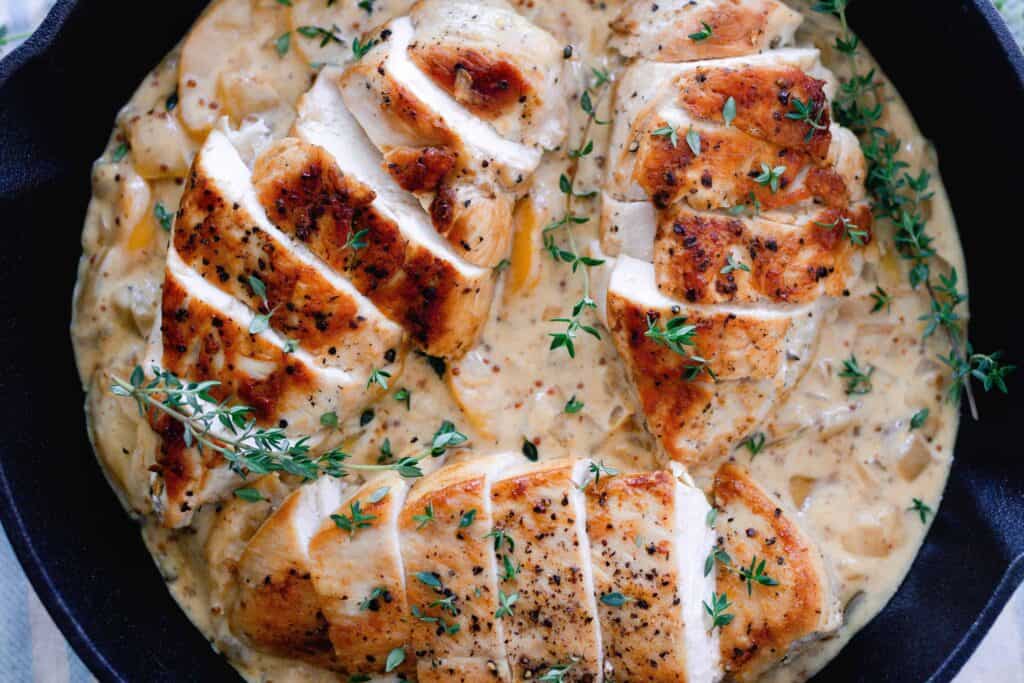 overhead photo of seared and sliced chicken breasts on top a creamy peach sauce with fresh sprigs of thyme