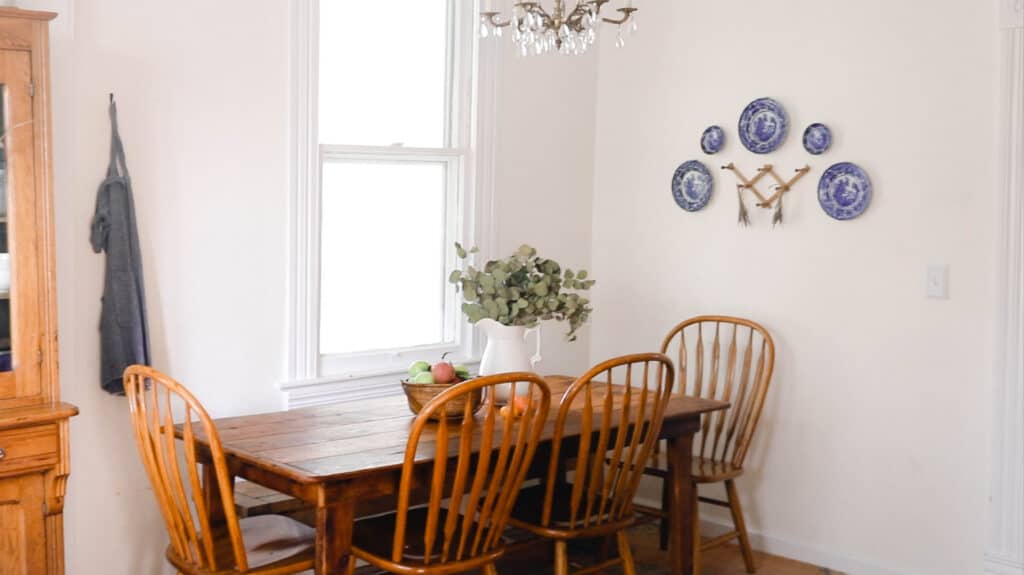 farmhouse table with 4 wooden chairs with a pitcher of eucalyptus and a basket full of hand picked apples