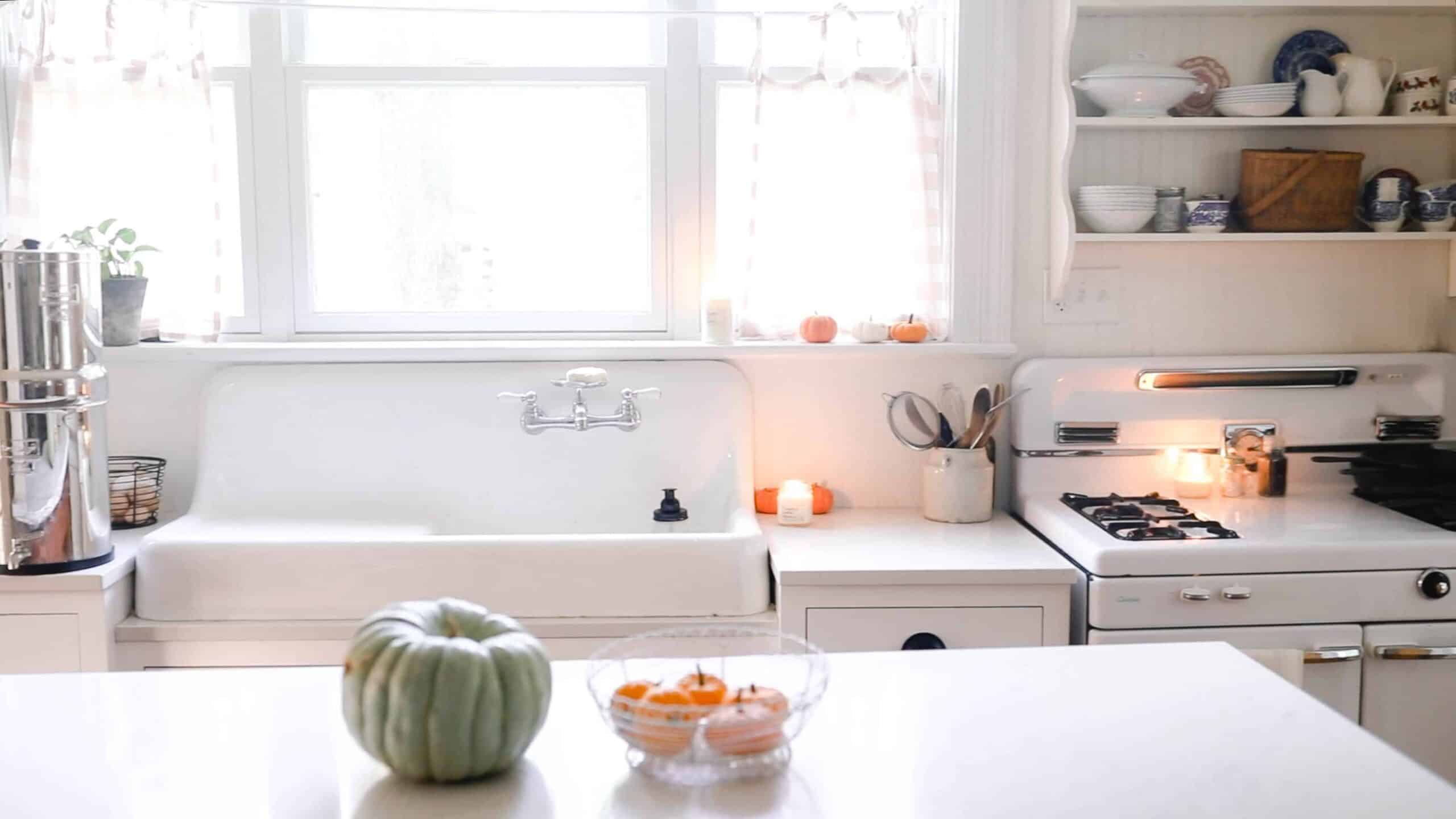 white victorian farmhouse kitchen with pumpkins set in a basket on the island and resting on the window sill